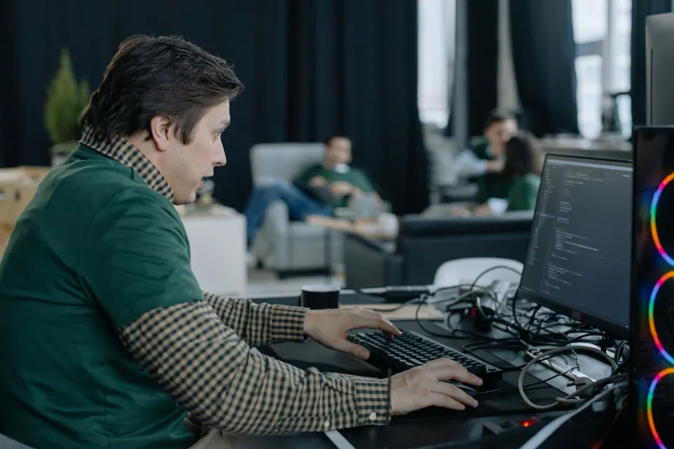 Softwareentwickler arbeitet an Code vor mehreren Bildschirmen im gedämpften Büro