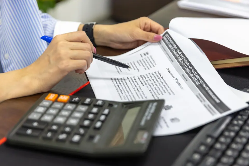 Hände mit Stift, Taschenrechner und Unterlagen am Schreibtisch